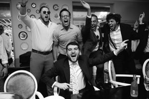 Monochrome image of a group celebrating with energetic expressions and raised arms in an indoor setting.