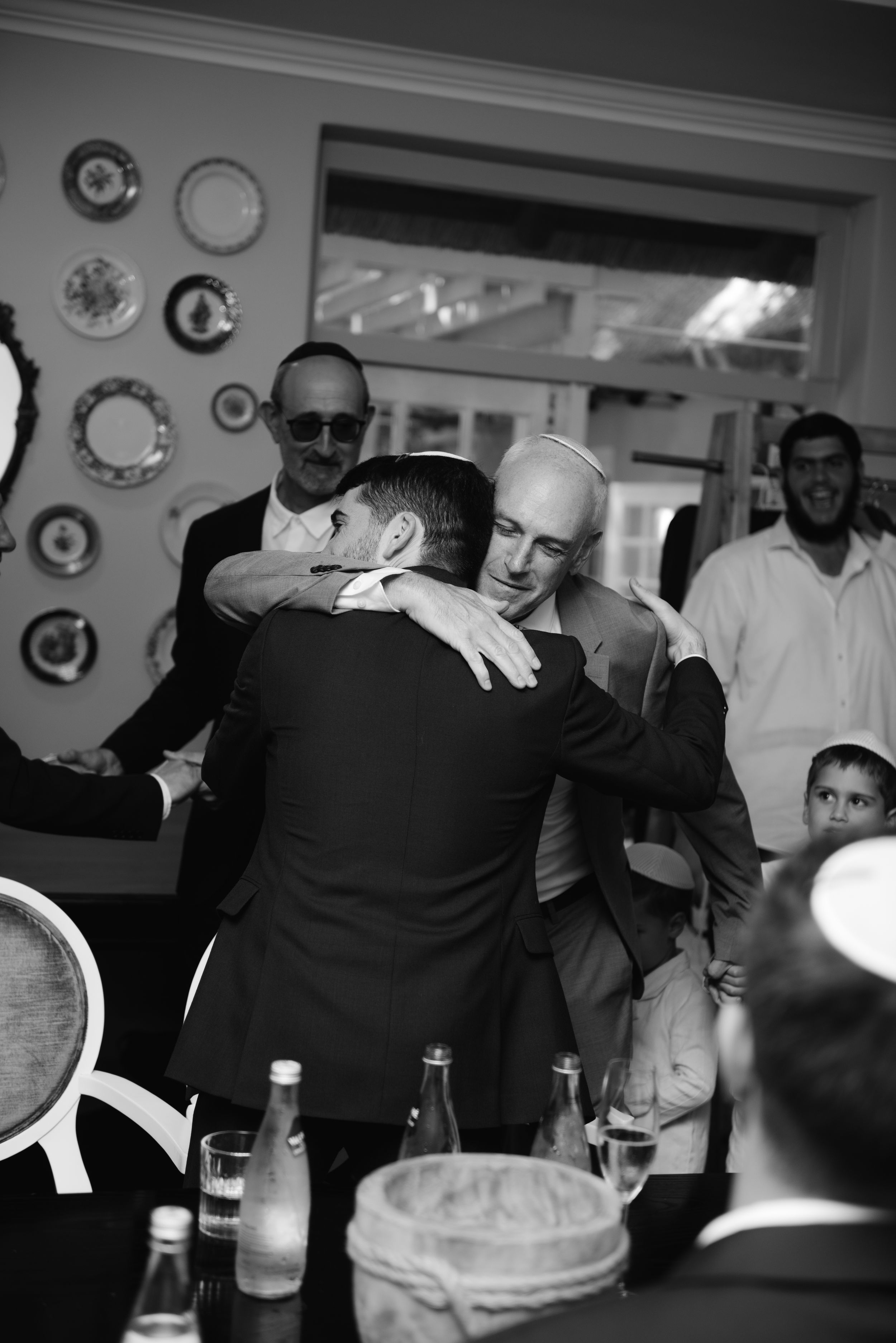 Black and white photograph capturing a social gathering with decorative plates on walls and people mingling.