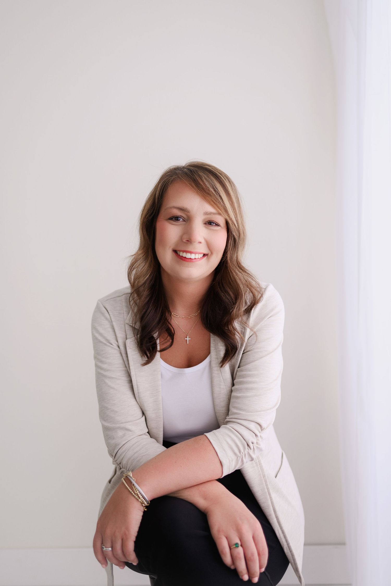 Cheerful female photographer with red-highlighted hair sitting on a stool holding a camera, wearing ripped denim jeans.
