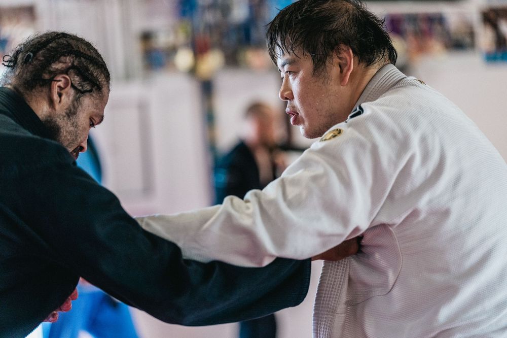 Two martial artists practicing jiu-jitsu techniques on a blue training mat.