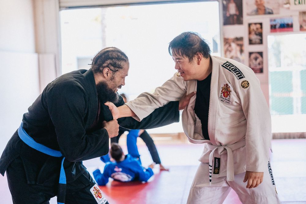Two martial artists practicing techniques together on a red mat in a training studio.