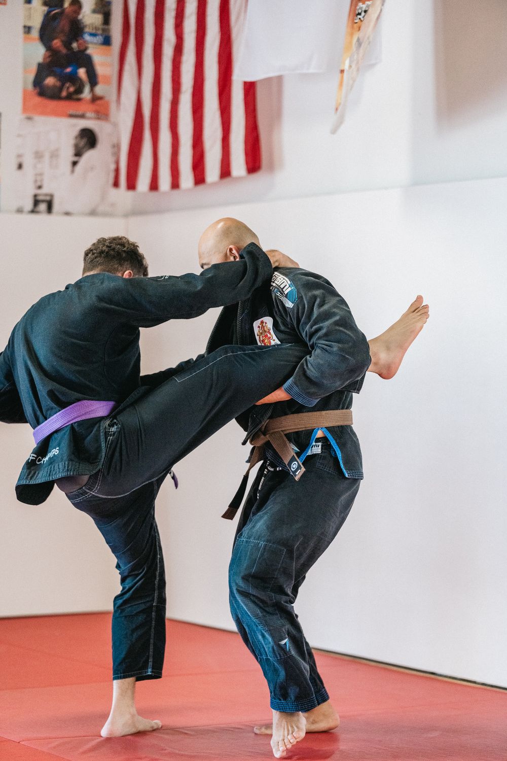 Two martial artists demonstrate a sequence of defensive moves on a red mat in front of American flags.