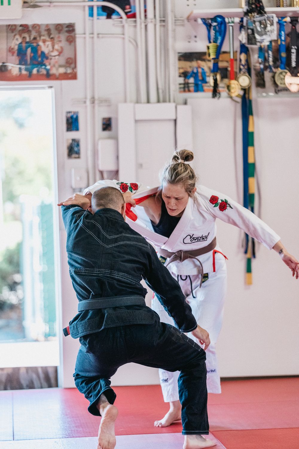 Two martial artists sparring in a dojo, one in white gi and one in black gi practicing kicks and blocks.