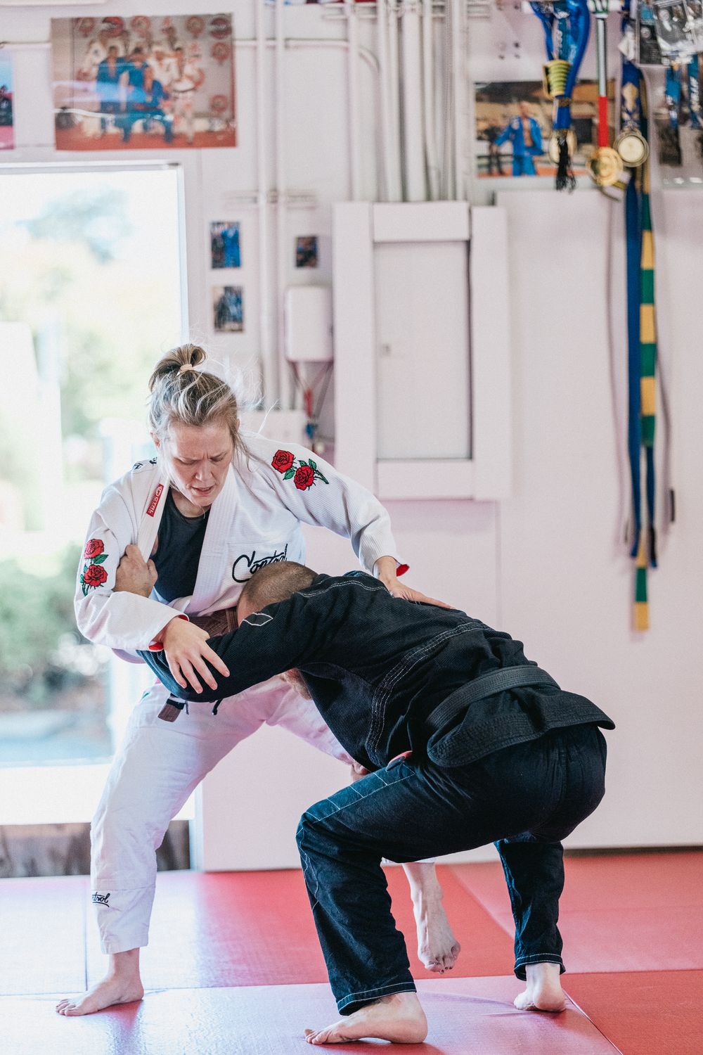 Two martial artists practicing judo throws and takedown techniques on red training mats.