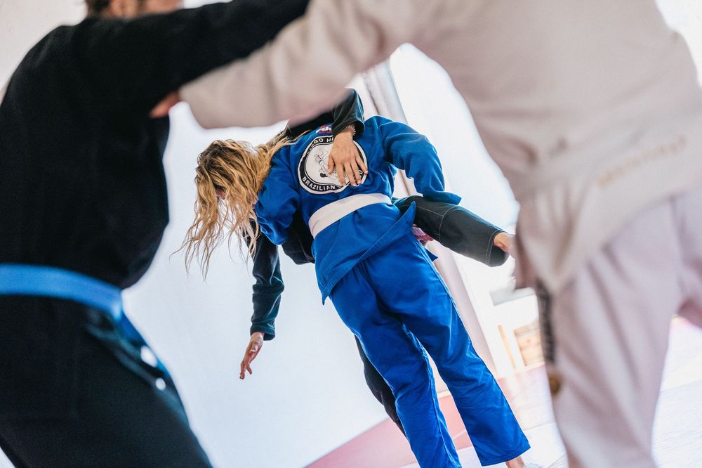 A person in a blue judo uniform performs a dynamic throwing technique during martial arts practice.