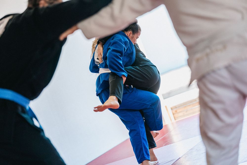 Martial arts students performing synchronized rolling techniques during training on red floor mats.