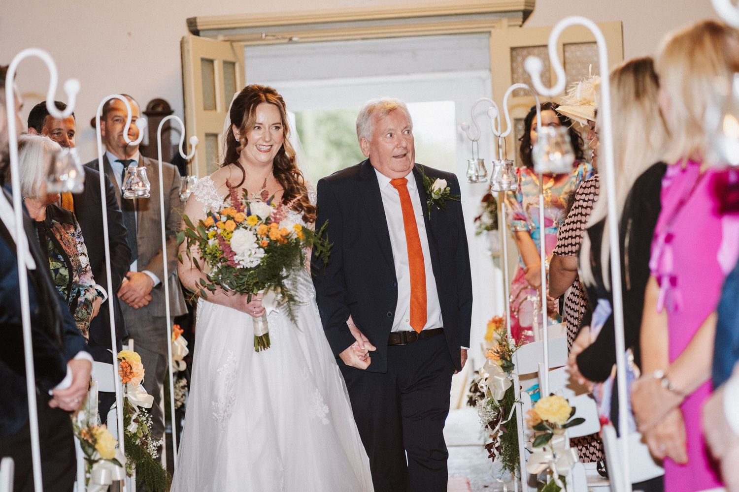 Wedding reception guests mingle and celebrate in an elegant indoor venue with bright decor and floral arrangements.