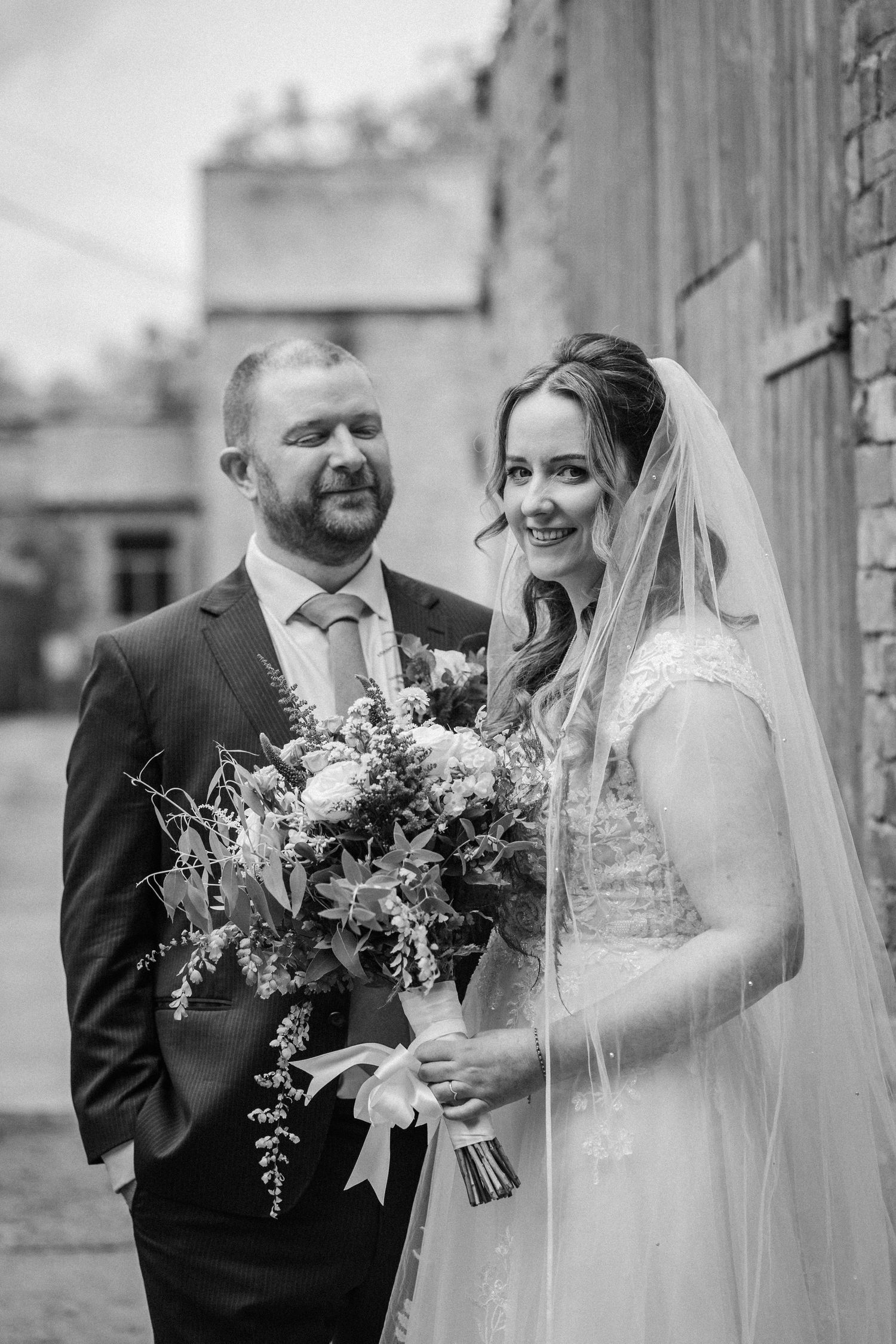 Wedding couple poses for portraits with beautiful floral bouquets against stone architecture.