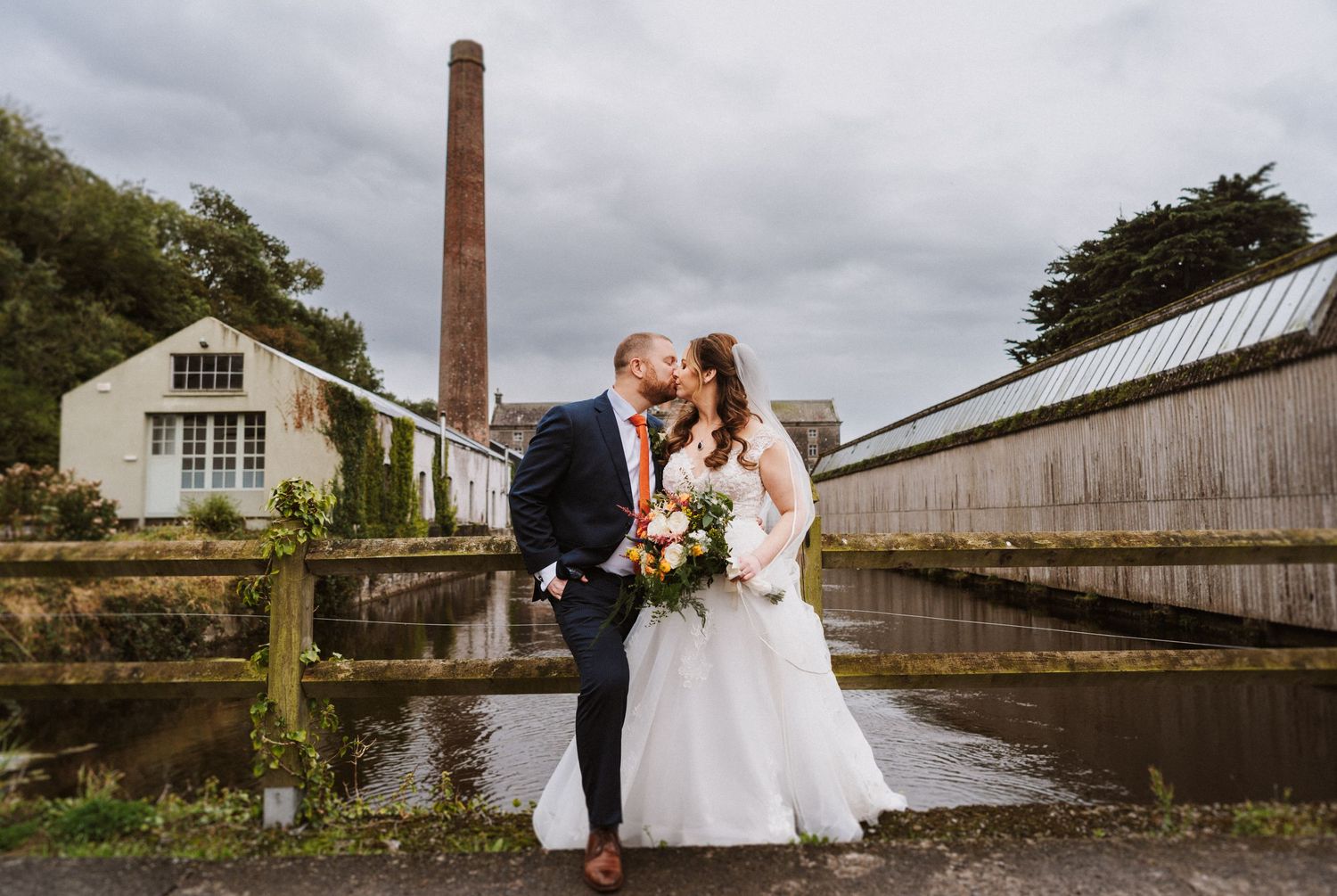 Wedding couple poses for romantic photos near industrial brick chimney and buildings.