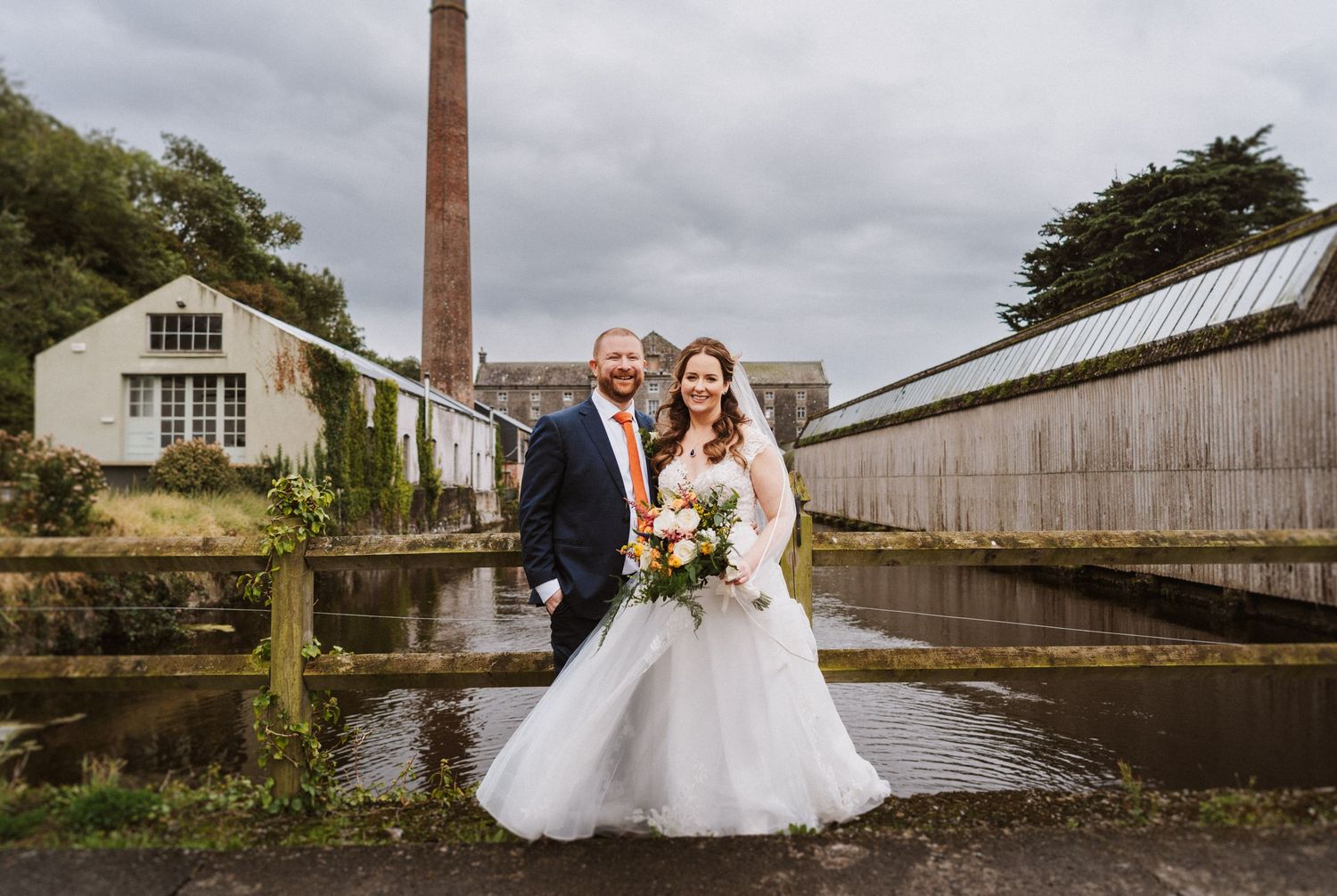 Industrial brick building and greenhouse structures create a rustic backdrop for outdoor wedding photos.