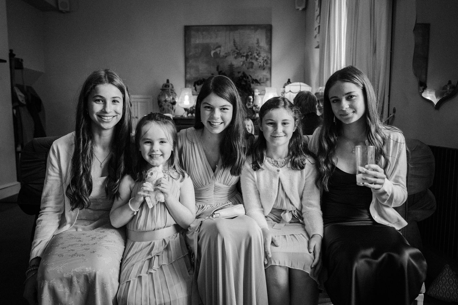 Bridesmaids in light colored dresses share candid moments while getting ready in a sunlit room.