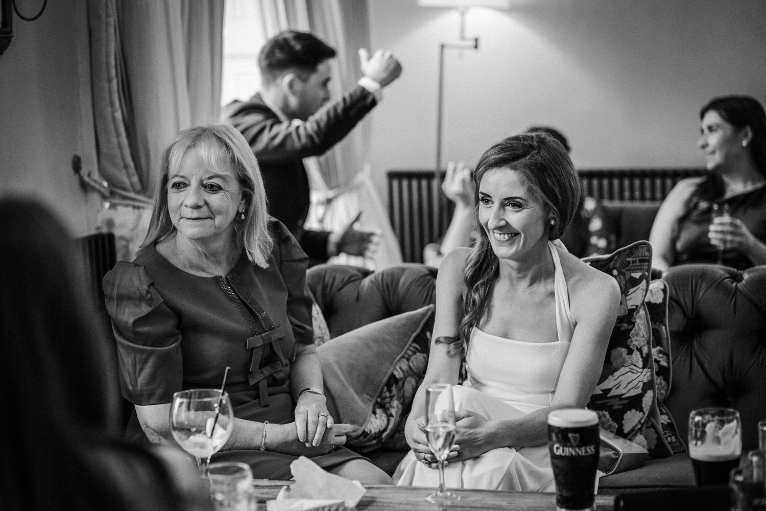 Wedding reception guests enjoy drinks and conversation at indoor tables.