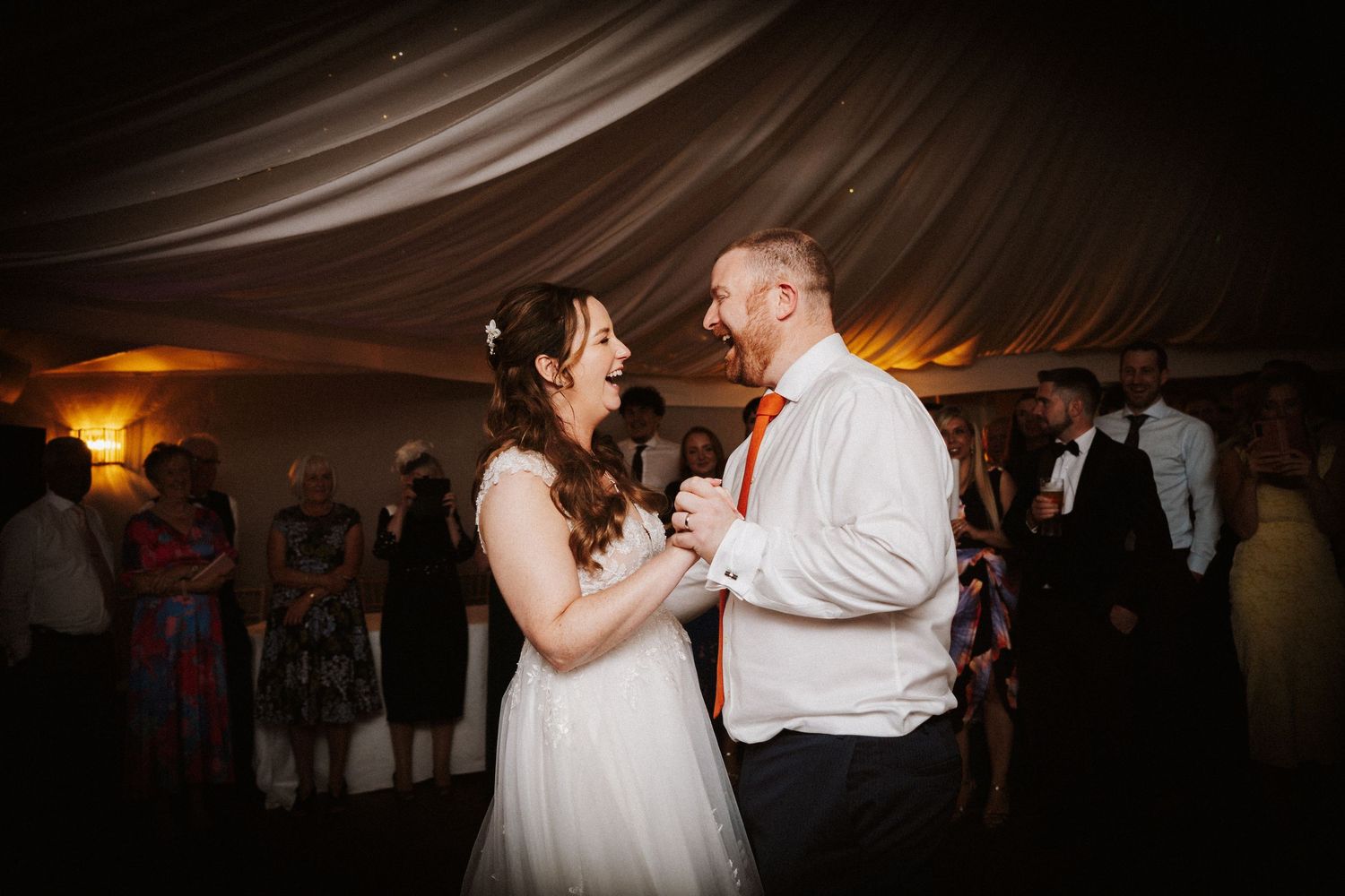 Romantic first dance moments captured in a dimly lit reception tent with warm ambient lighting.
