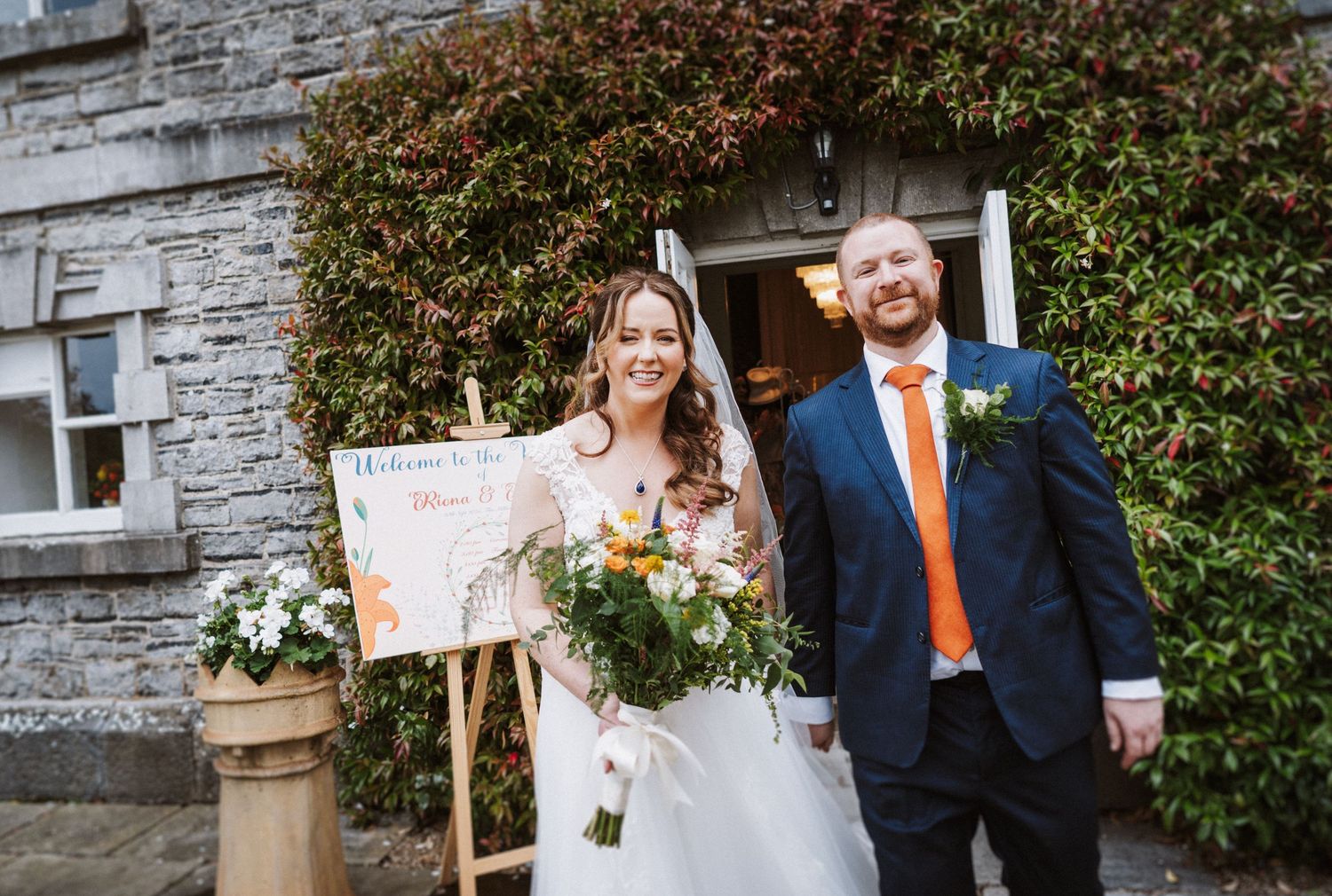 Wedding couple poses against rustic stone wall with autumn foliage in the background.