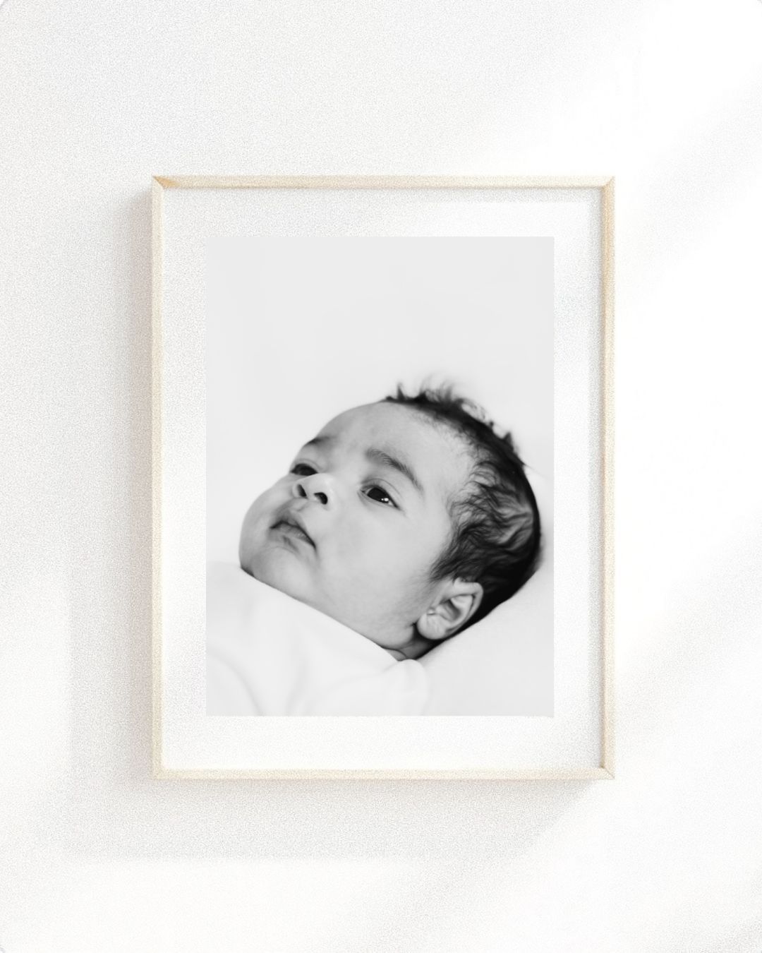 Black and white framed portrait photograph of a baby looking upward against a white background during newborn shoot in Nottingham