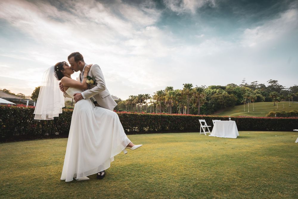A romantic wedding couple shares an intimate moment on a grassy field at sunset.