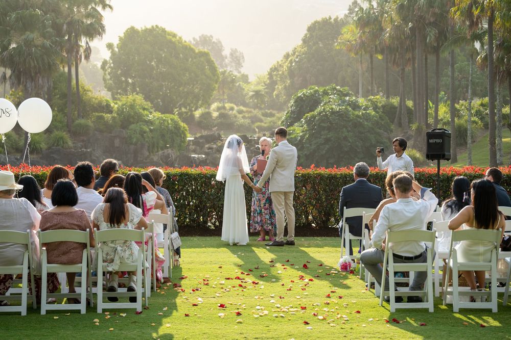 Outdoor wedding ceremony setup with white chairs on a grassy lawn surrounded by trees at sunset.