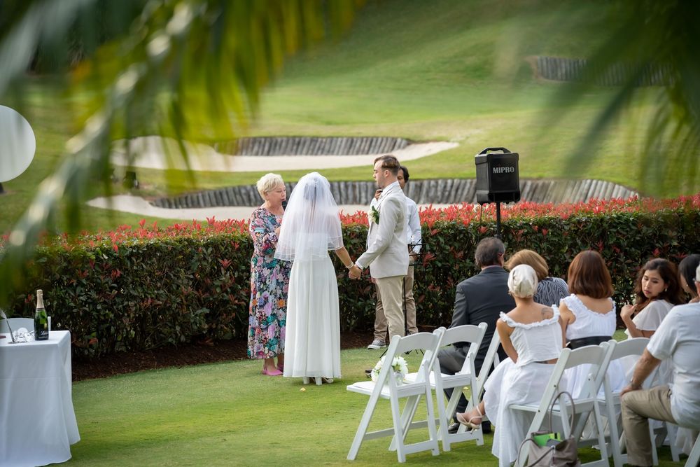 Wedding ceremony setup with white chairs and decorations on a lush green lawn surrounded by tropical landscaping.