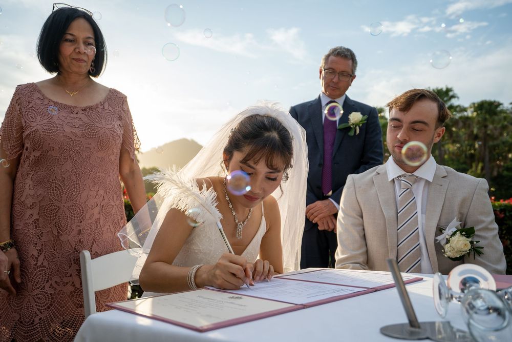 People signing documents at a formal event while others observe the proceedings.