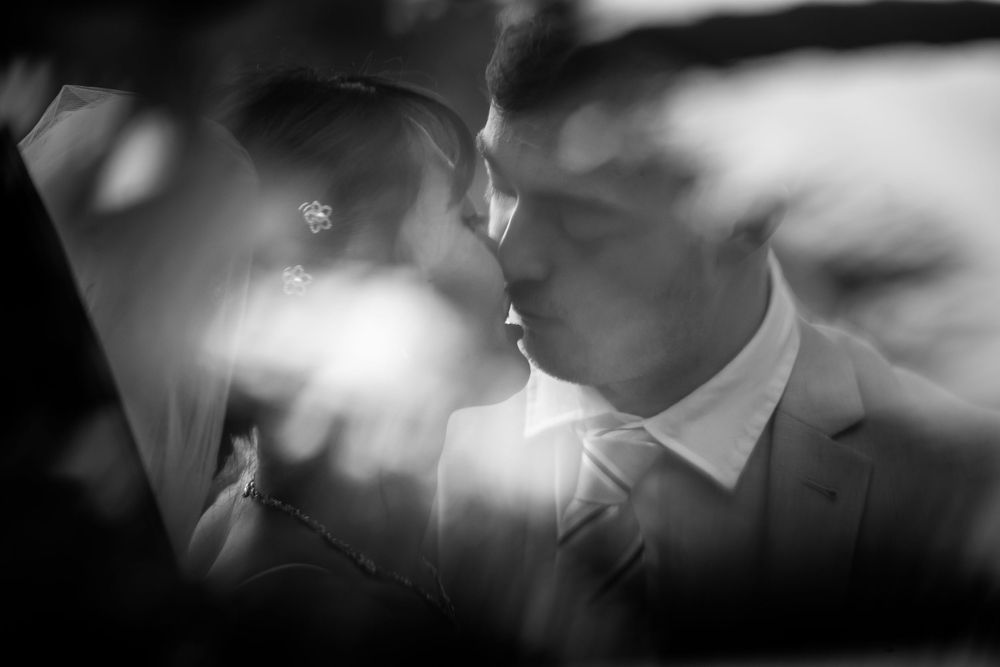 A romantic black and white wedding photo capturing an intimate moment between a couple in soft lighting.