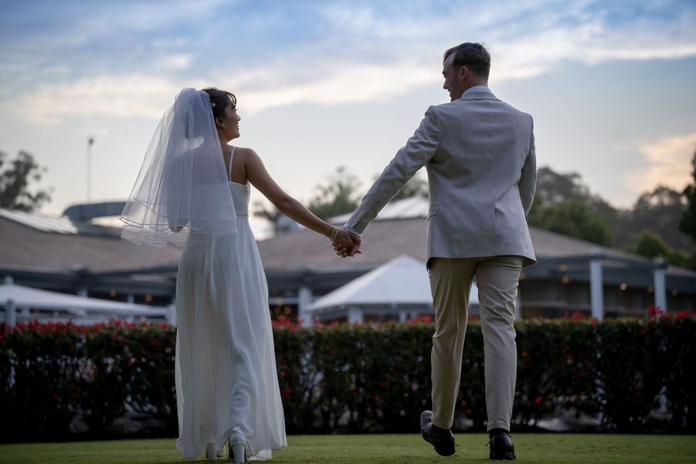 Newlyweds share a joyful dance outdoors with white tents and greenery in the background.