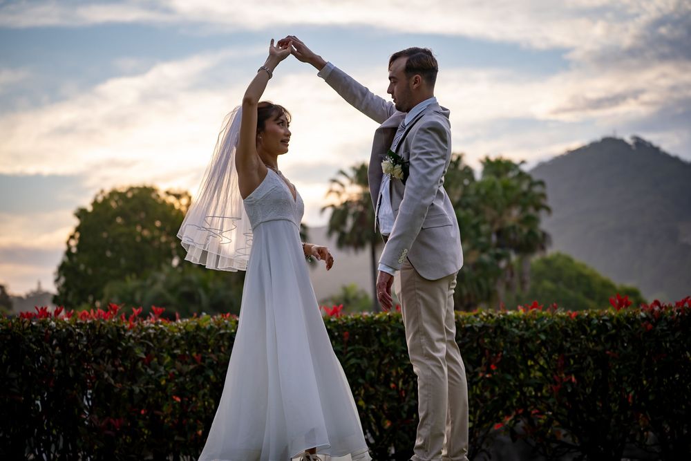 A couple dances together in an outdoor garden setting with mountains and sunset in the background.