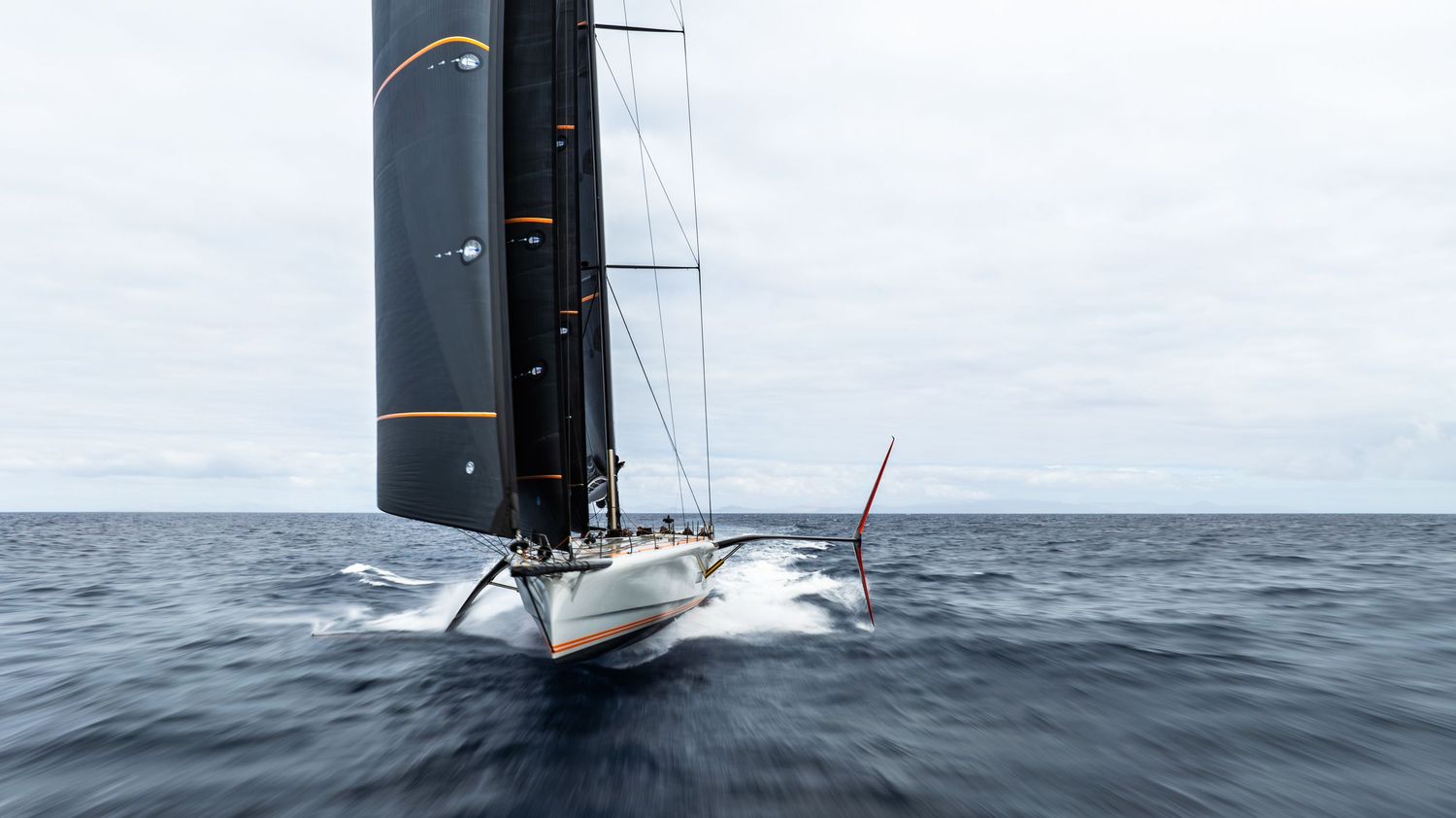 Modern racing yacht with black sails cutting through rough ocean waters.