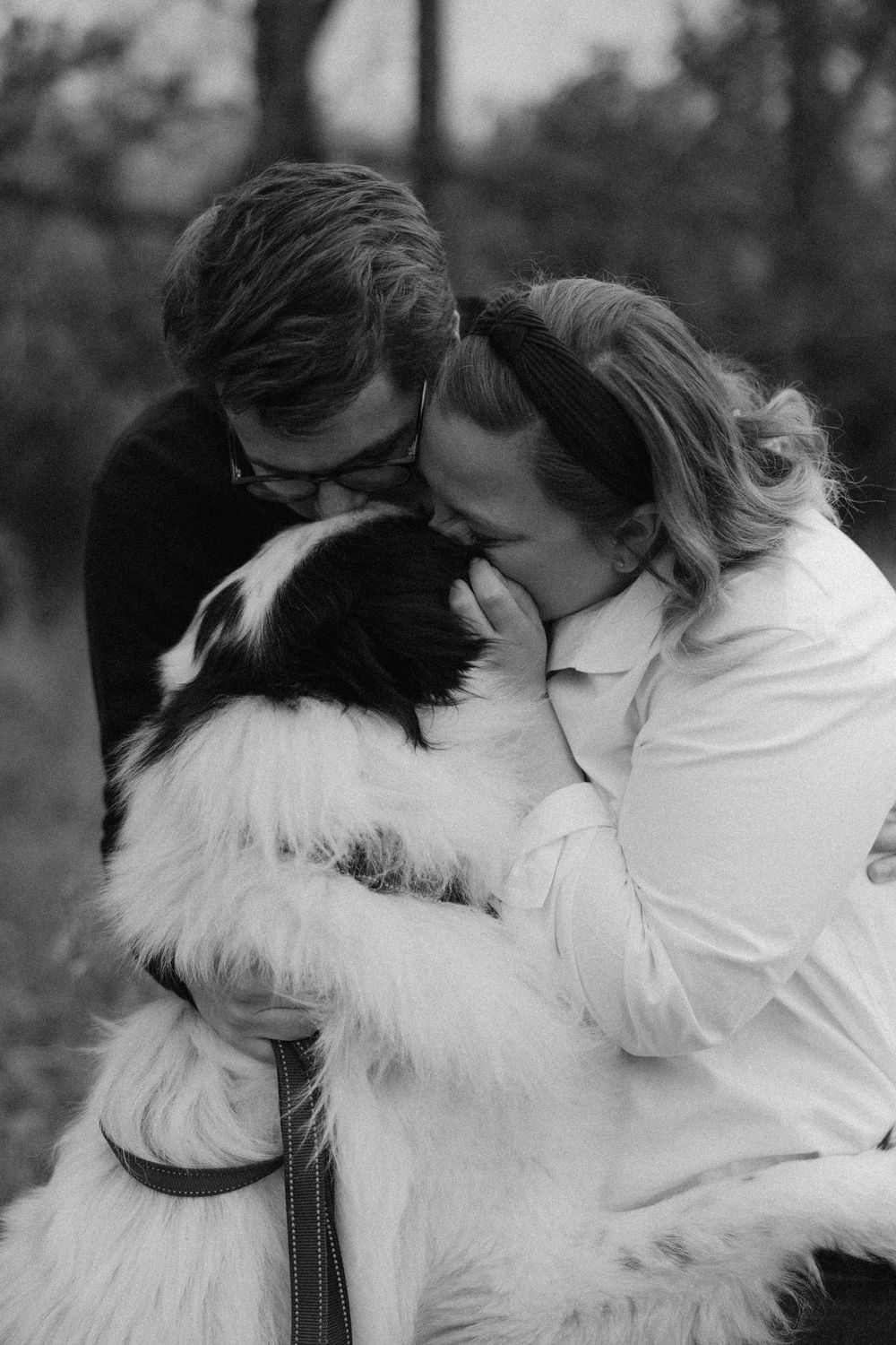 A tender moment shared between a couple and their fluffy white dog in black and white.