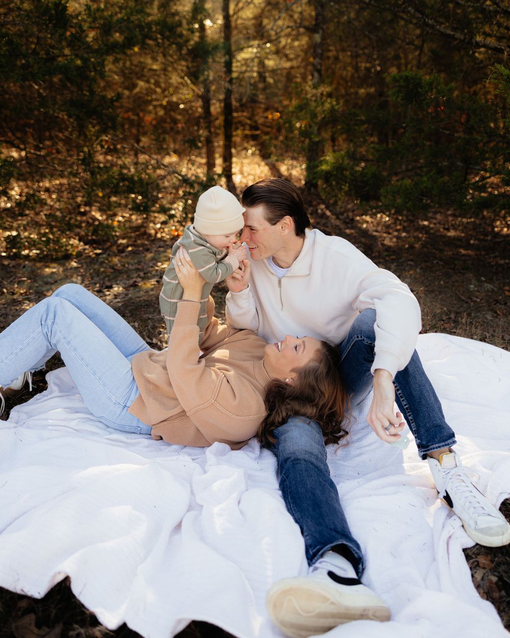 Couple lying on white blanket in autumn forest setting during outdoor photoshoot.