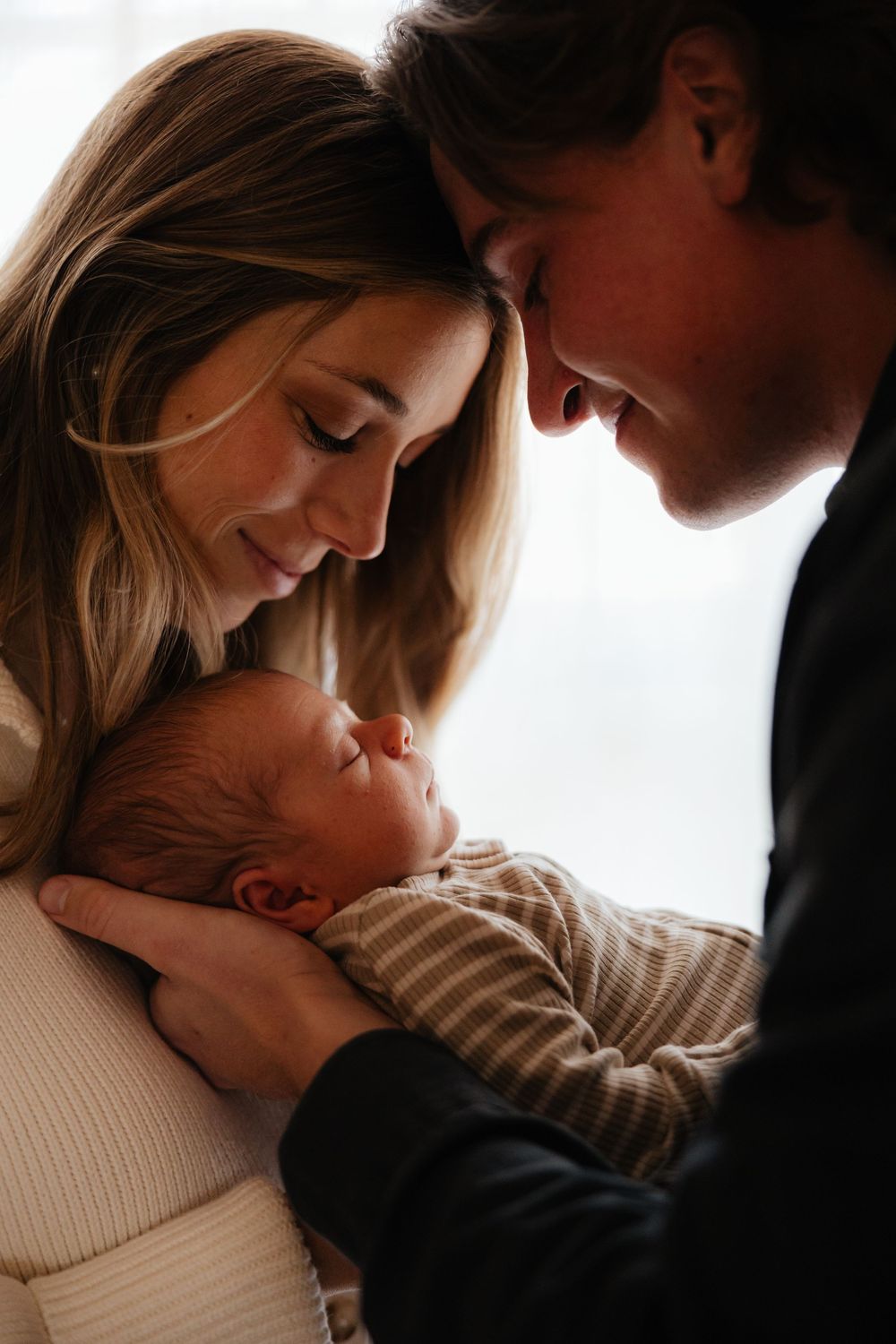 Intimate indoor family portrait in soft window light with gentle expressions.