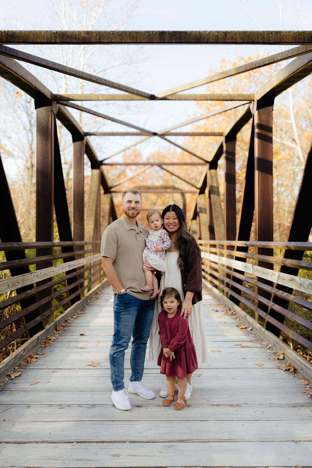 Family portrait on wooden bridge during autumn with rustic metal beams overhead.