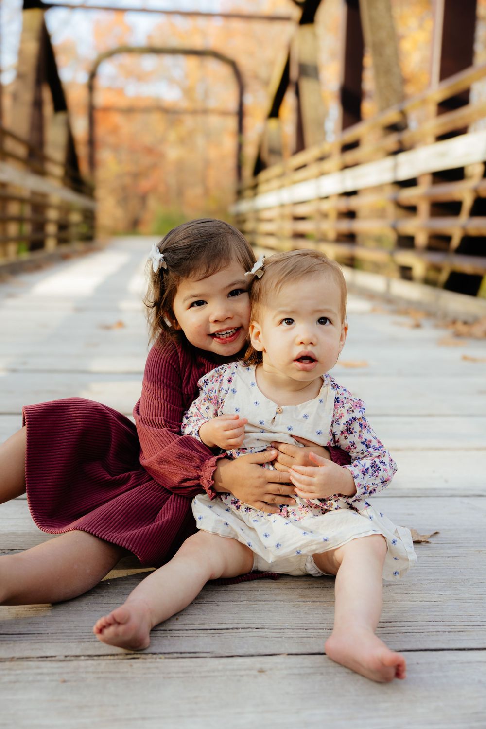 Two young children sitting together on wooden bridge during autumn photoshoot.