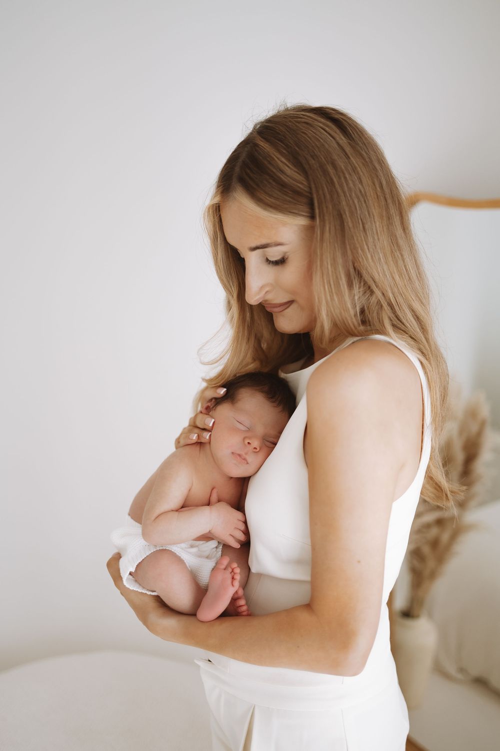 A tender moment captured in soft light as a mother in white cradles and embraces her sleeping newborn baby.