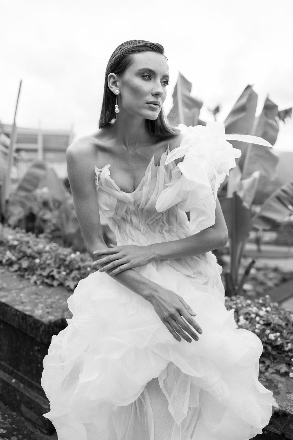 Artistic black and white fashion series showing model in flowing white dress against garden backdrop.