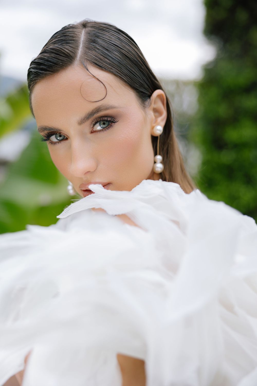 A close-up portrait with dramatic white feathers or fabric creating an ethereal effect against a blurred green background.