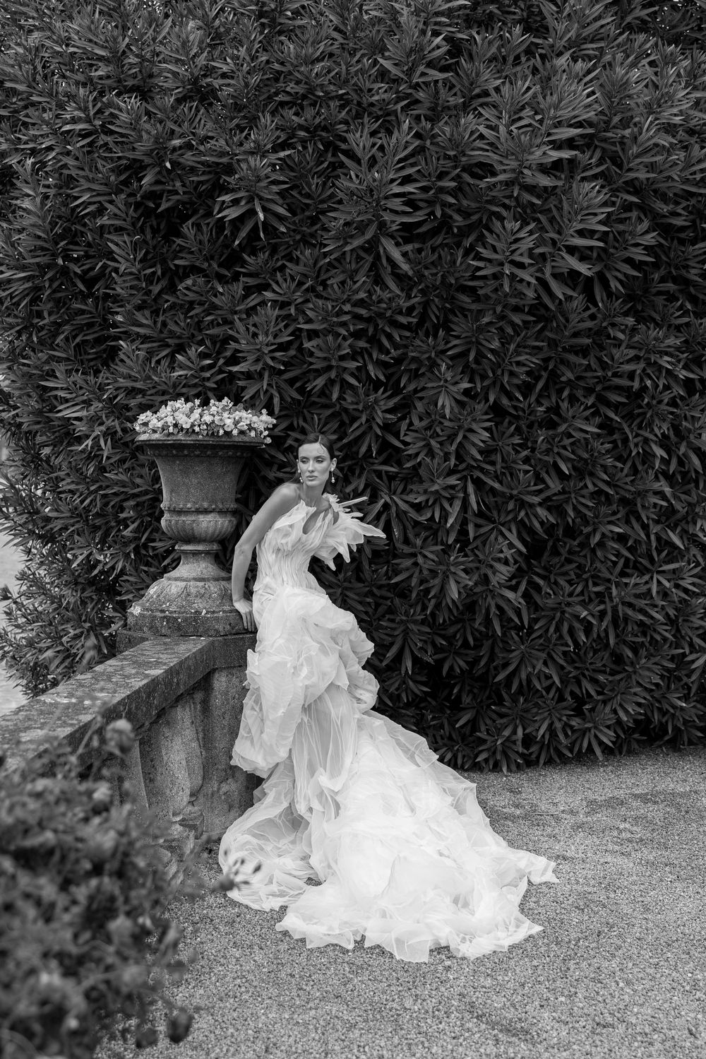 A black and white photo series shows a bride in a flowing white gown posing gracefully beside a garden urn.