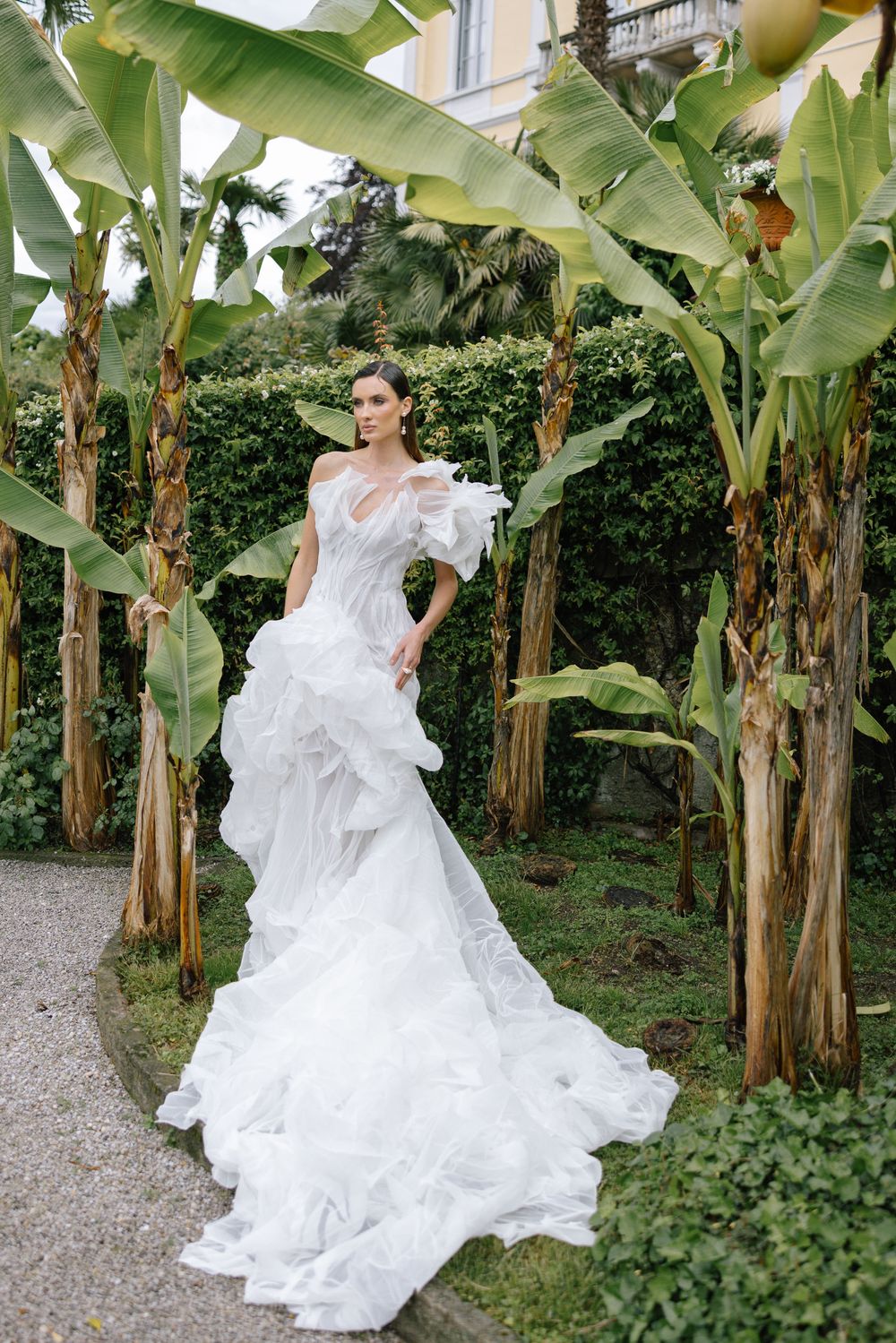 A bride in a flowing white wedding dress twirls gracefully among banana trees in a lush garden setting.