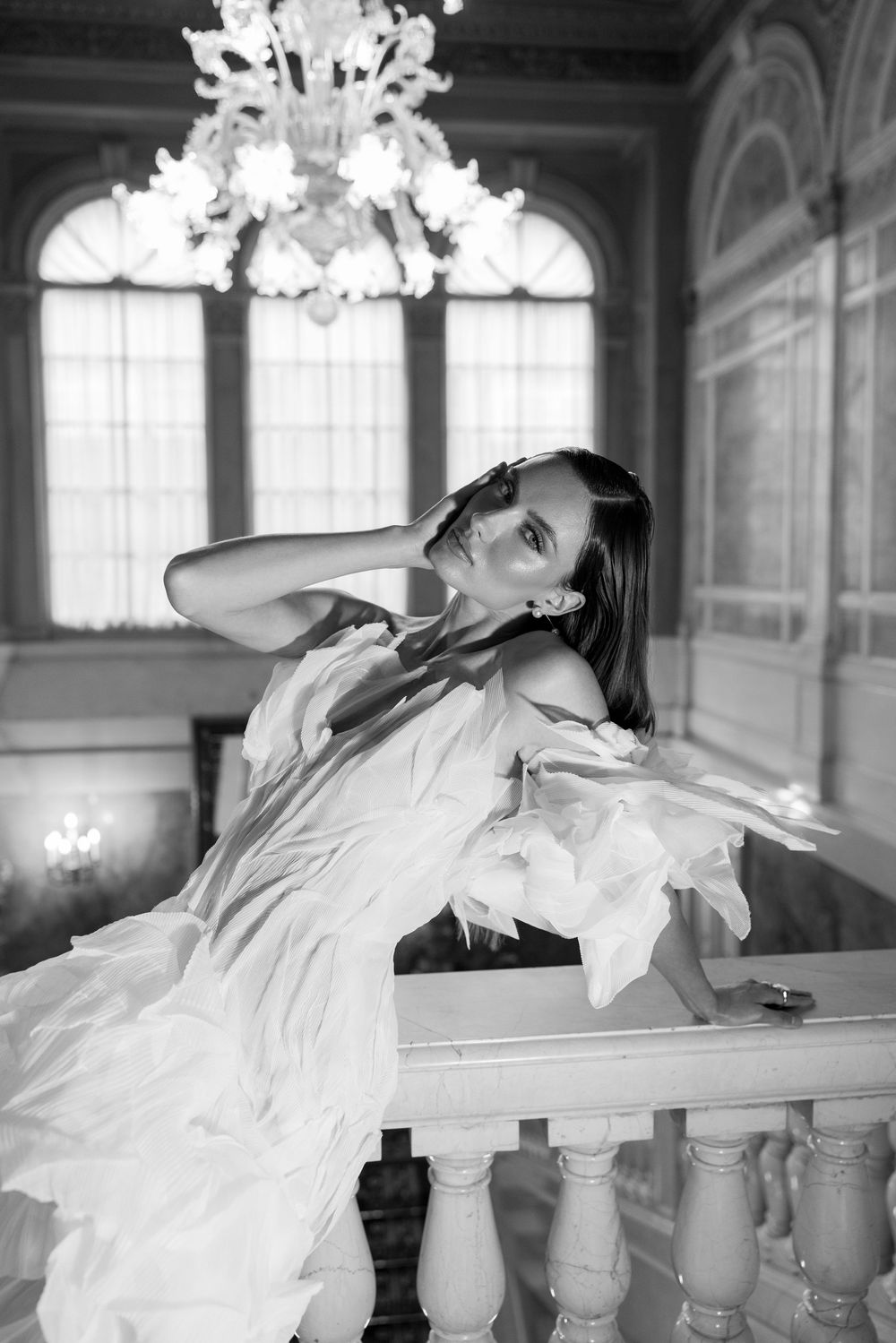 A series of black and white photos showing a dancer in a white dress gracefully posing along an ornate balustrade.
