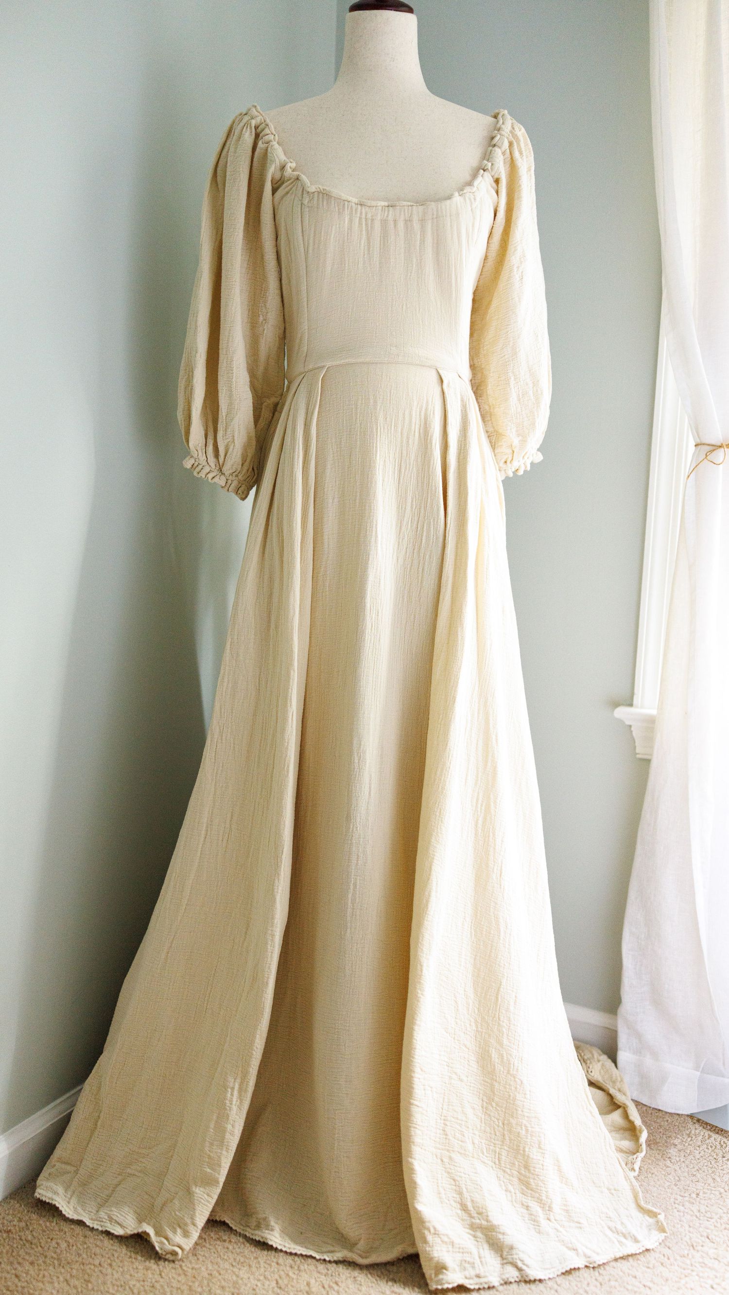 Vintage cream-colored maxi dress with puff sleeves and gathered neckline displayed on white mannequin against pale wall.