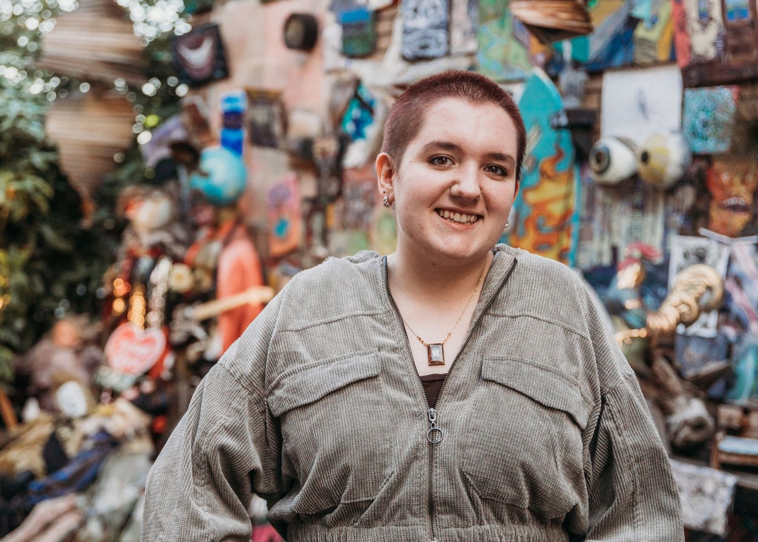 Someone wearing a gray utility jacket smiles while standing in front of a colorful wall display of decorative items.