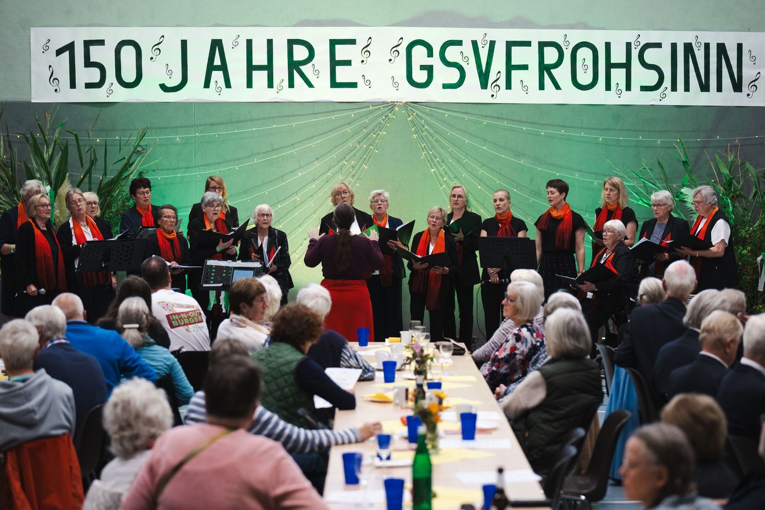A group of people stand together at a formal event with green lighting and banners in the background.