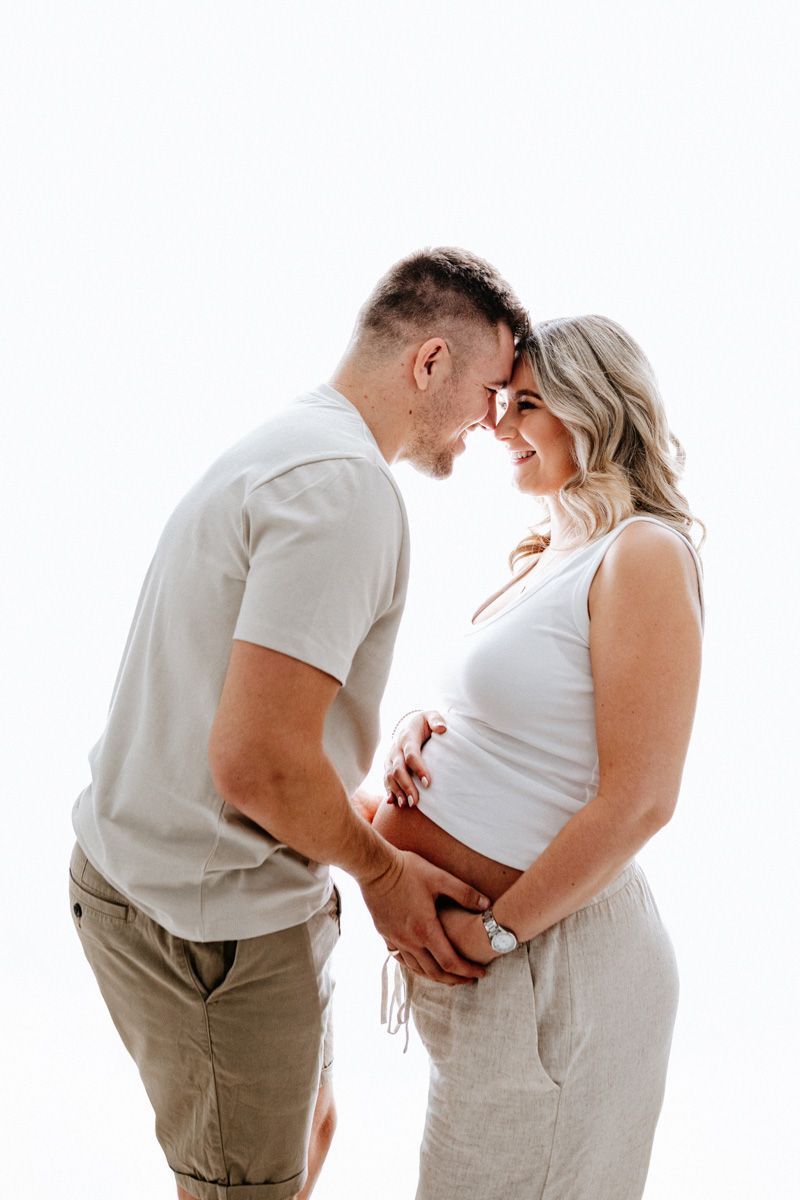 A series of three pregnancy progression photos showing a couple in white tops and khaki pants touching their growing belly.