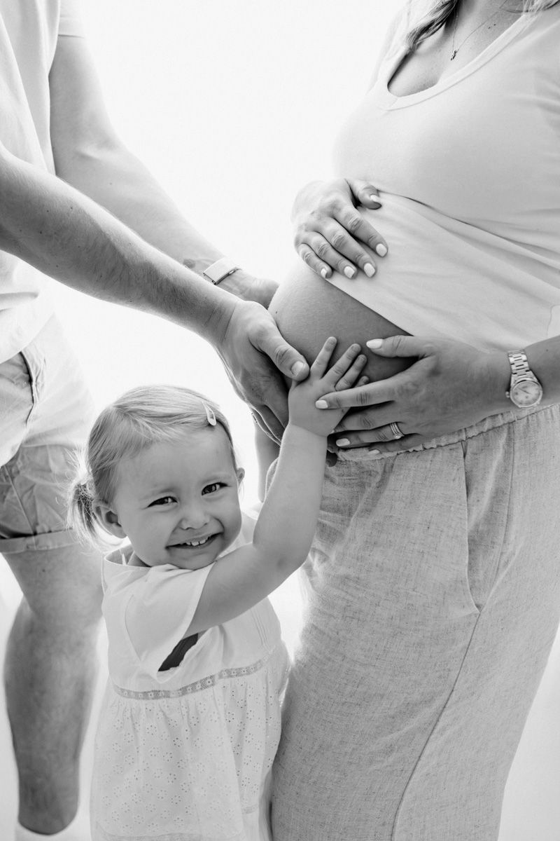 A creative pregnancy progression photo series showing a growing baby bump in white clothing against a light background.