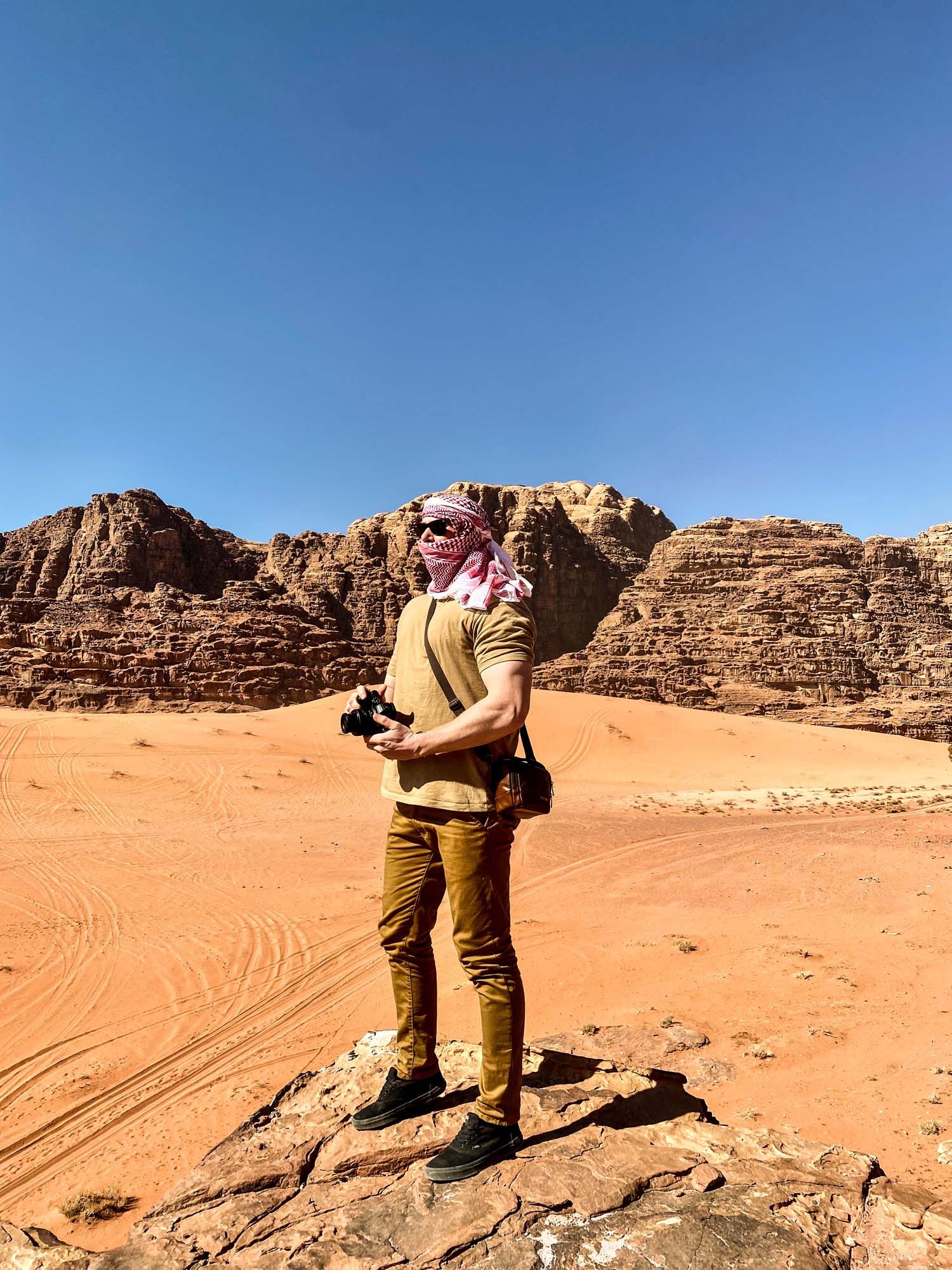 A panoramic view of red sand dunes and towering sandstone cliffs in Wadi Rum desert, Jordan under clear blue skies.