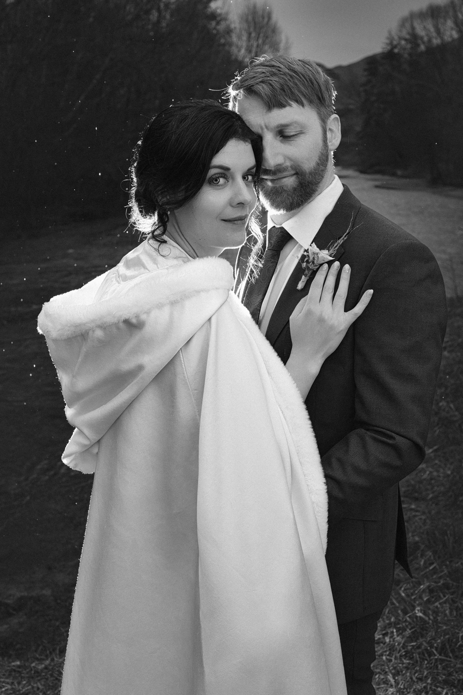 Intimate black and white portrait of newlyweds sharing tender moment outdoors.