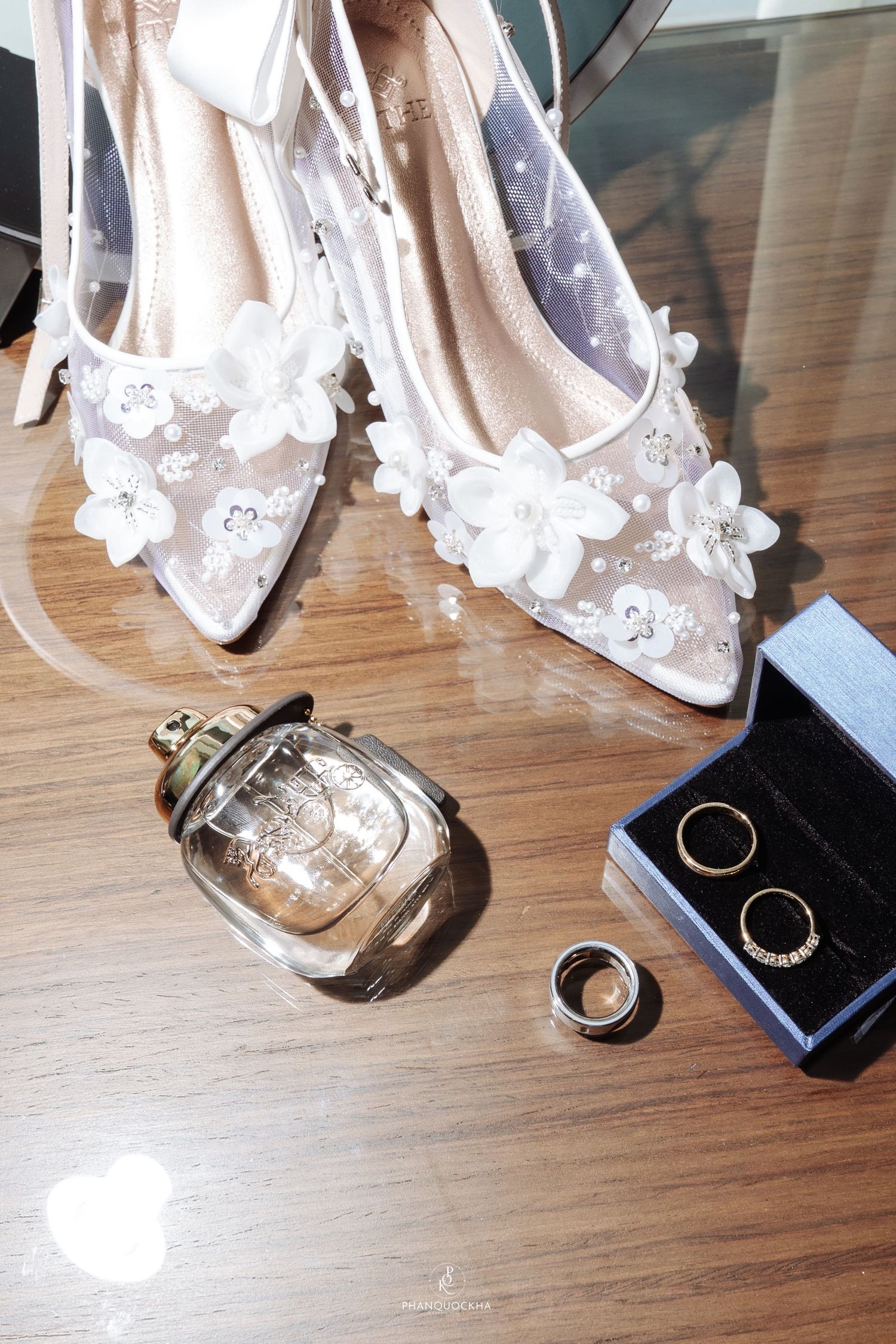 Bridal accessories flat lay featuring lace floral heels, perfume bottle, wedding bands, and diamond earrings.