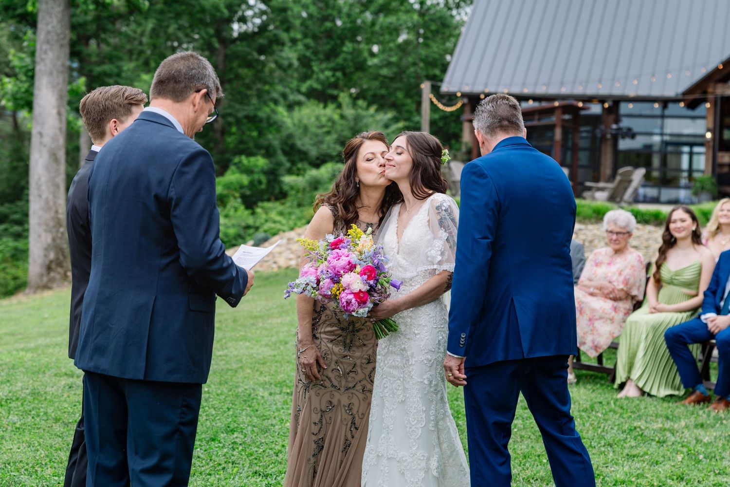 Indoor wedding ceremony under an elegant green floral arch with wedding party and guests gathered in bright sunlit venue.