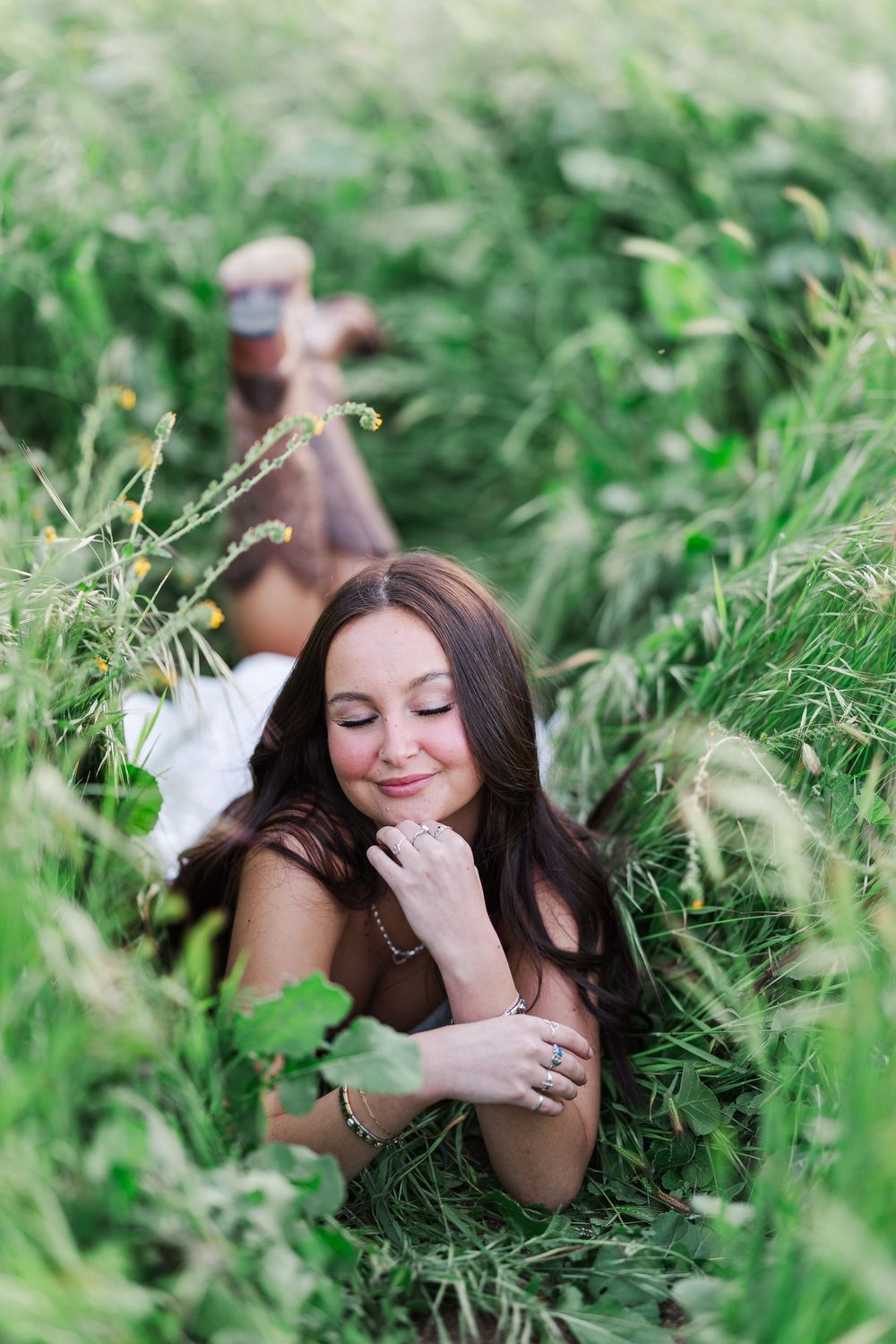 A person lies peacefully in tall green grass wearing a white feathered accessory.