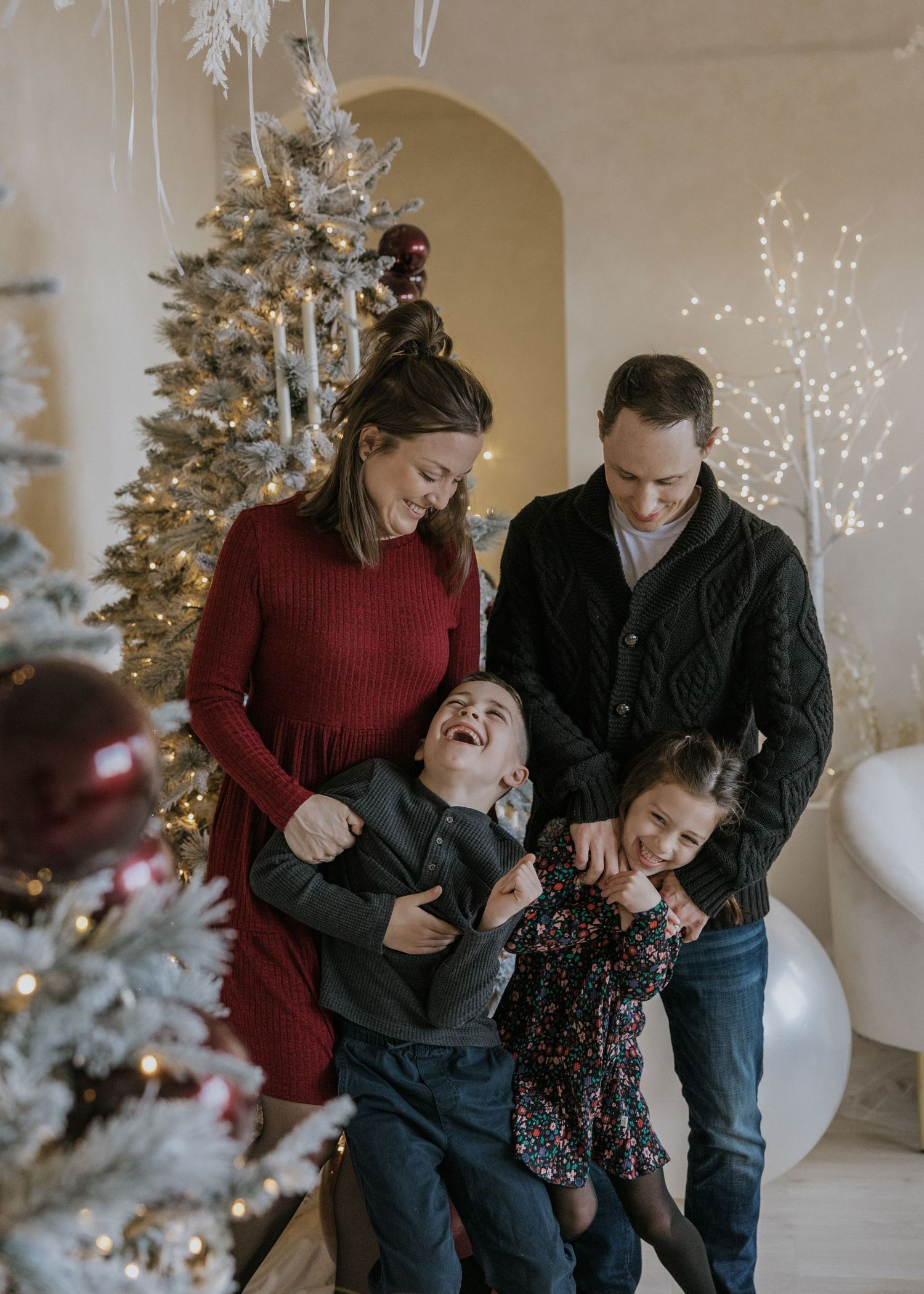 A family shares joyful laughter together in front of a decorated Christmas tree during a holiday photoshoot.