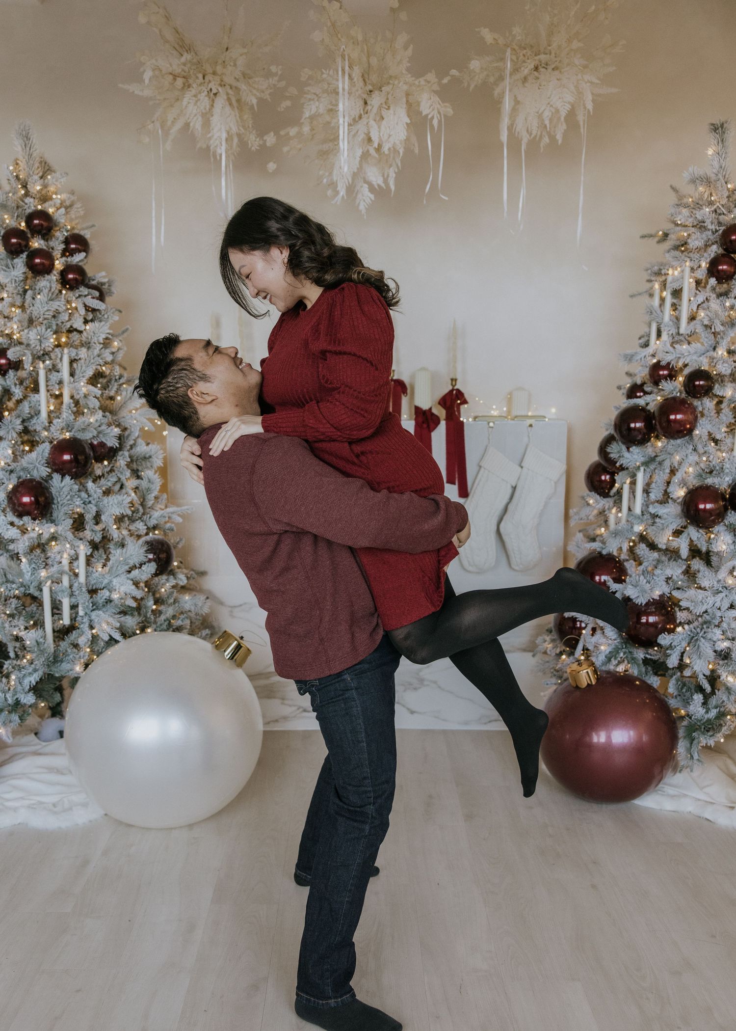 A romantic holiday moment with a couple embracing in front of white Christmas trees and decorative ornaments.